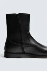 Bota de caña media fabricada en piel color marrón oscuro, con cierre de cremallera lateral, horma cuadrada y suela con ligero tacón.
