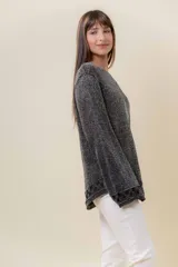Sweater de tejido liviano con efecto lurex, color beige o gris claro metalizado. Presenta cuello redondo, mangas amplias estilo campana y terminaciones en punto elástico con diseño de cuadros en puños y ruedo.