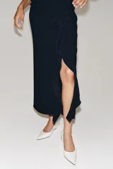 Vestido midi de cuello redondo y manga corta, confeccionado en tejido fluido color azul marino. Presenta un diseño con detalle de drapeado y volado lateral en la parte delantera, con cierre en la espalda mediante abertura y botón.