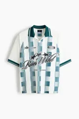 Camiseta de fútbol de manga corta en malla estampada, color blanco con diseño a rayas verticales en tono verde y detalles gráficos en el pecho. Cuenta con cuello abierto verde con finas rayas blancas y corte holgado.