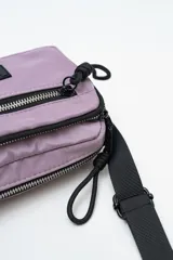 Cartera tipo bandolera de nylon color lila, con cierre frontal y correa ajustable negra.