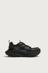 Zapatilla deportiva tipo running de color negro, confeccionada con una combinación de materiales y piezas, con suela robusta de gran volumen y diseño irregular.