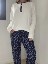 Pijama de algodón compuesto por una remera blanca de manga larga con cuello redondo, botones frontales y ribete con detalle estampado, acompañado de un pantalón azul marino con estampado floral y cordón ajustable en la cintura.