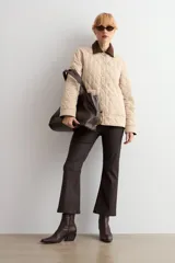 Campera capitoneada de diseño acolchado con patrón de rombos, color beige claro. Presenta cuello camisero de pana en color marrón oscuro, cierre frontal con botones metálicos y bolsillos frontales de parche.