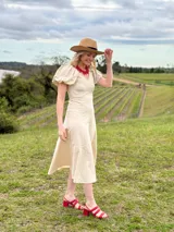 Vestido midi beige de IneGug, de corte entallado en el torso con recortes verticales que estilizan la figura y falda con vuelo y bajo asimétrico. Posee escote en V y mangas cortas globo con volumen.