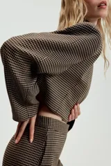 Blazer corta de corte recto con estampado de cuadros pequeños en tonos marrones y negros. Presenta cuello solapa, manga larga y cierre frontal con un botón.