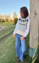 Chaleco tejido en mohair con diseño de guarda geométrica en la parte superior. Presenta una combinación de colores gris, blanco y beige, con cuello redondo y corte recto.