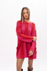 Buzo tipo poncho de tejido de punto con diseño de bloques de color en tonos rojo y fucsia. Presenta un corte oversize muy amplio, cuello redondo, mangas largas y bolsillos laterales integrados.