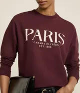 Saco de algodón color bordó con cuello redondo y mangas largas. Tiene ribete en cuello, puños y bajo. Estampado frontal con la leyenda "Paris - Champs Élysées - Est. 1965".