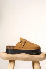 Zueco de plataforma color camel, confeccionado en material tipo gamuza, con detalle de hebilla metálica lateral y base de corcho con suela de goma negra.