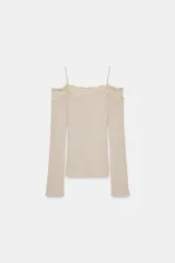 Camiseta color beige de escote recto y hombros descubiertos, con tirantes finos y manga larga. Presenta un detalle de encaje a tono en el escote y está confeccionada en tejido rib.