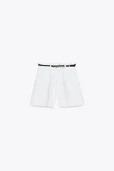 Shorts blancos de tiro alto con pinzas delanteras y bolsillos laterales. Incluye un cinturón fino negro con hebilla de cadena dorada.