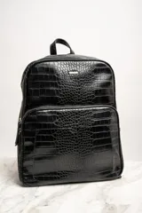 Mochila negra con textura símil cuero de cocodrilo, con dos compartimentos principales con cierre y asa de mano en la parte superior.