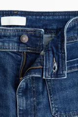 Jean de denim azul de corte acampanado y tiro alto, con bolsillos parche delanteros y traseros.