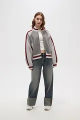Campera de punto con cierre frontal, cuello alto y diseño de rayas laterales en mangas. Presenta un patrón texturizado en el cuerpo y detalles de rib acanalado en puños, cuello y ruedo.