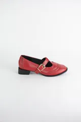 Zapato tipo guillermina estilo oxford, confeccionado en cuero negro con detalles de perforaciones decorativas en la puntera y cierre mediante tira con hebilla metálica dorada. Presenta un taco bajo cuadrado.