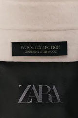 Chaqueta de lana en color beige, con cuello solapa, cierre frontal con cremallera metálica, mangas largas con corte evasé y bajo asimétrico.