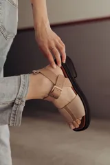 Sandalia de cuero color tostado con tiras anchas, tira en el talón y hebilla metálica rectangular ajustable. Cuenta con suela de goma con tacón bajo y plataforma.