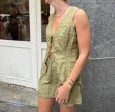 Conjunto de dos piezas color verde oliva con textura arrugada. Incluye un chaleco sin mangas con cierre frontal de lazos y una minifalda ajustada.