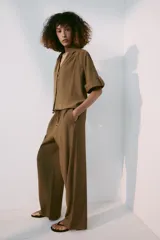 Pantalón de tiro medio color marrón, con cintura elástica y cordón ajustable con abalorios decorativos. Presenta bolsillos laterales y perneras rectas con diseño texturizado.