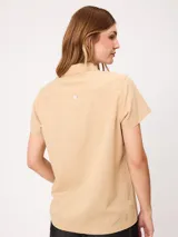 Camisa de manga corta color beige, confeccionada en mezcla de algodón y lino, con cuello camisero, cierre frontal de botones y dos bolsillos aplicados en el pecho.