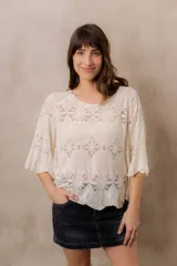 Blusa de punto calado color blanco, con diseño geométrico y floral transparente, escote redondo y mangas tres cuartos amplias de calce relajado.