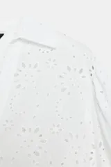 Camisa blanca con cuello solapa, escote pico y mangas tres cuartos abullonadas con elástico en el puño. Presenta bordados perforados (ojales) con diseño floral en toda la prenda.