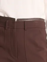 Pantalón de corte recto y entallado, estilo ankle, en color marrón. Presenta cintura con detalle en cuero sintético, pasadores funcionales, cierre frontal con broche y bolsillos delanteros.