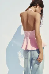 Top rosa claro, entallado, con cuello halter que se abrocha en la nuca y espalda descubierta. El bajo tiene un corte peplum acampanado.