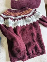 Sweater tejido a mano en mohair, con diseño de canesú con patrón geométrico en tonos bordó, blanco y naranja. Presenta cuello redondo, mangas largas y puños acanalados.