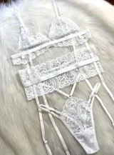 Conjunto de lencería de cuatro piezas en color blanco, confeccionado en encaje con diseño floral. Incluye bralette triangular, tanga de tiro alto con tiras ajustables, portaligas integrado y ligas para las piernas.