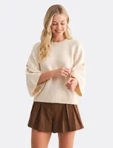 Buzo de punto beige con mangas tres cuartos anchas, cuello redondo y detalle de botones en las mangas.