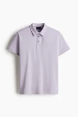 Remera polo de manga corta color lila claro, confeccionada en punto de algodón liviano, con cuello y tapeta de botones. Presenta un corte ajustado al cuerpo.