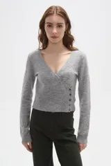 Sweater de punto gris con cuello en V, diseño cruzado y cierre lateral con botones. Presenta mangas largas y un ajuste al cuerpo con detalle acanalado en la cintura.