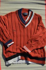 Buzo tejido de punto con escote en V, manga larga y diseño holgado. Presenta un patrón de rayas verticales en relieve y detalles de franjas en contraste en el cuello, puños y ruedo. Incluye un pequeño bordado en el pecho.