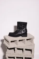 Bota corta negra de cuero con hebillas y arnés metálico.