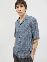 Camisa de manga corta con estampado geométrico en tonos azul y beige, cuello resort y cierre de botones. Confeccionada en tejido dobby 100% algodón.