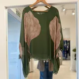 Blusa verde oscuro semitransparente con gran estampado de hojas en tonos beige y marrones, cuello redondo y mangas amplias y fluidas.