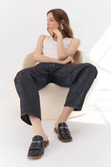 Mocasín abierto de cuero color crema con detalle de hebilla metálica plateada y flecos en el empeine.