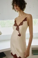 Vestido mini tipo lencero de tejido satinado color crema, con escote en pico y tirantes finos. Presenta detalles de encaje a contraste en color bordó en el escote y en el ruedo.