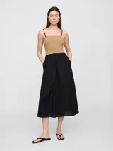 Vestido midi con diseño bicolor, presenta un cuerpo ajustado en color beige con breteles finos negros y una falda amplia de corte evasé en color negro con bolsillos laterales.