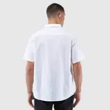 Camisa de manga corta con cuello clásico, cierre frontal de botones y un bolsillo en el pecho. Presenta un diseño de corte regular con textura natural.