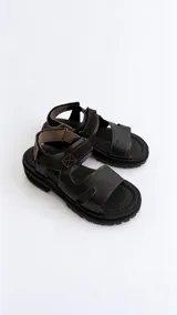 Sandalias negras de cuero con tiras anchas, suela track y cierre con tira ajustable de velcro en el empeine y el talón.