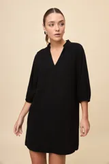 Vestido corto negro de silueta relajada, con escote en V y mangas 3/4 levemente abullonadas.