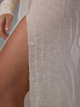 Saco largo de punto color blanco, confeccionado en 100% lana merino natural, con diseño jacquard de ramas, cuello alto, cierre frontal con pequeños botones y aberturas laterales.