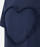 Remera marrón de algodón con cuello redondo y mangas cortas. Presenta un aplique de corazón con volados en el frente.