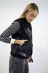 Chaleco gamulán marrón de efecto cuero con interior y detalles de corderito sintético en cuello, solapas y bordes. Cuenta con cierre frontal, bolsillos laterales con cierre y tiras con hebilla en el bajo.