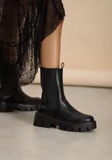 Botas tipo Chelsea de caña media, color negro, con paneles elásticos laterales y suela de plataforma dentada. Presentan un diseño minimalista con tirador en la parte superior trasera.