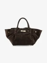 Cartera tipo tote de diseño amplio y estructurado, confeccionada en gamuza color marrón oscuro. Presenta asas cortas, laterales con volumen y un cierre frontal con detalle metálico.