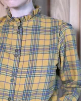Camisa de algodón con estampado de rayas verticales finas, cuello alto con volados, cierre frontal con botones dobles y mangas largas con puños elásticos terminados en volados.